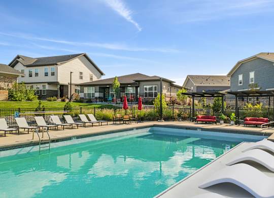 A swimming pool with lounge chairs and umbrellas in front of a row of houses.