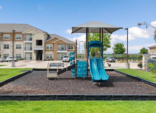 A playground with a blue slide and a brown building in the background.