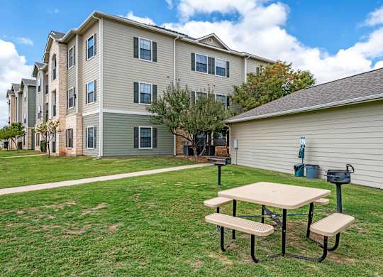 A picnic table is in the foreground of a grassy area in front of a building.