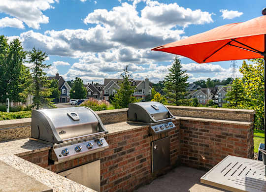 Two grills on a patio with a red umbrella above.