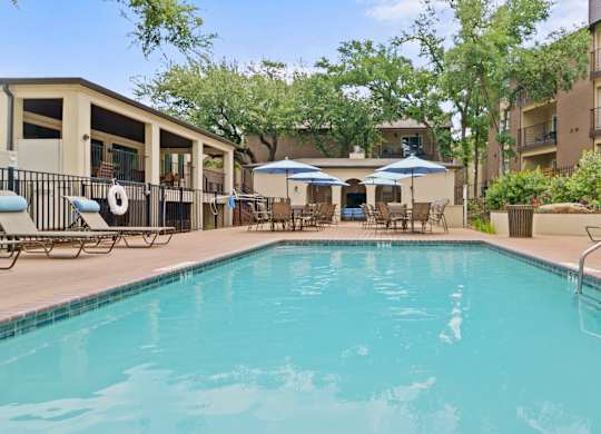 a swimming pool with lounge chairs and umbrellas in front of a building