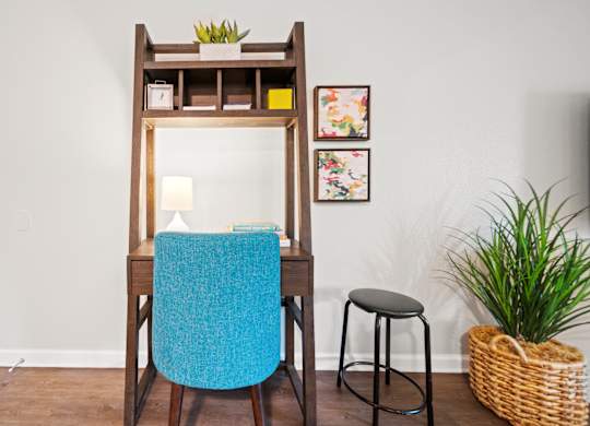 a desk with a blue chair and a black stool in a room with a white wall and