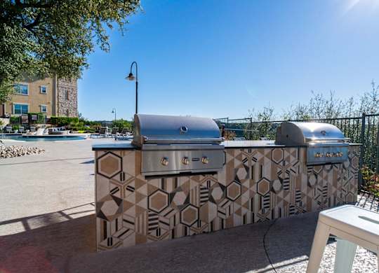 A large outdoor kitchen with a patterned tile backsplash and a grill.