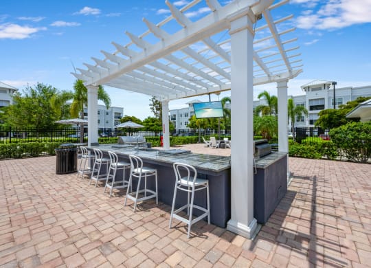 an outdoor bar with white columns and a white pergola on top of a brick patio