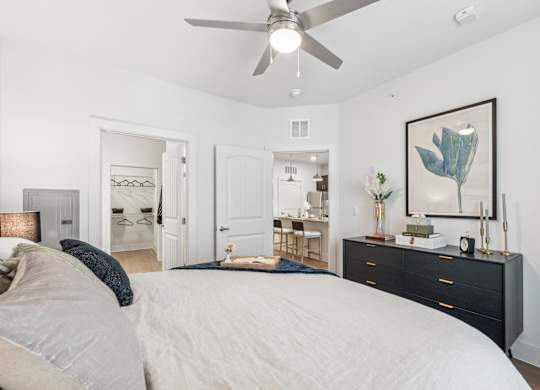 A bedroom with a large bed, a dresser, and a ceiling fan.