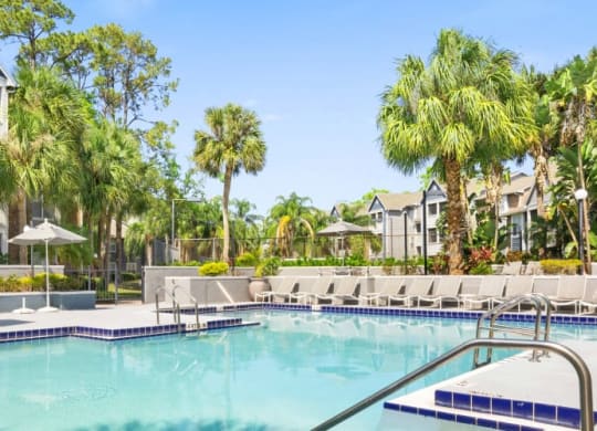 a large swimming pool with chaise lounge chairs and palm trees in front of a building