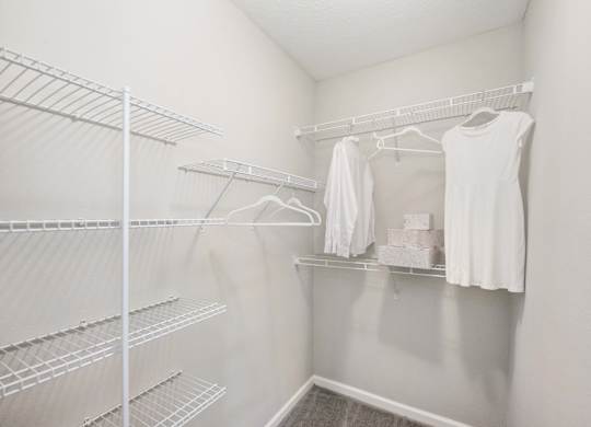 a walk in closet in a bedroom with white walls and a white dress hanging on the wall