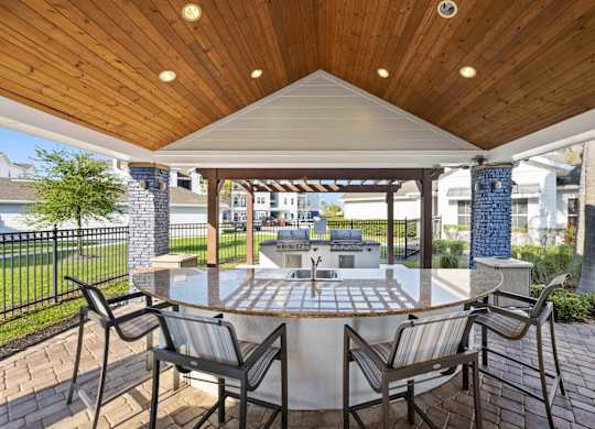 a patio with a large circular table and chairs with a grill in the background