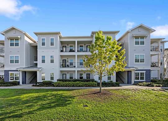 an apartment building with white siding and a tree in front of it
