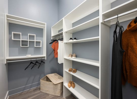 a walk in closet with white shelves and grey walls