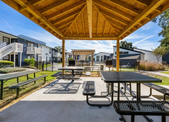 two picnic tables and benches under a pavilion at an apartment complex