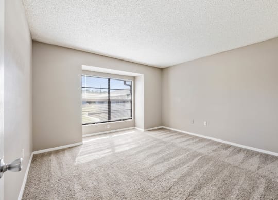 an empty living room with a window and carpeted flooring