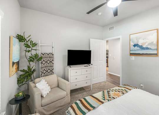 A bedroom with a bed, chair, and television.