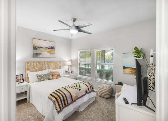 A bedroom with a bed, a ceiling fan, and a television.
