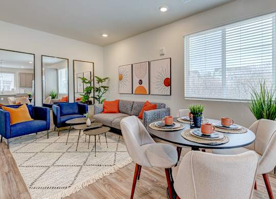 A modern living room with a grey sofa, orange pillows, and a round table with chairs.