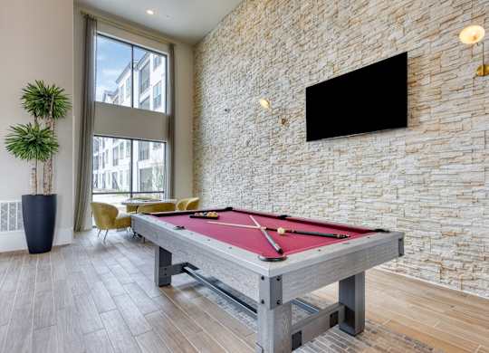 A pool table in a room with a brick wall and a flat screen TV mounted on it.