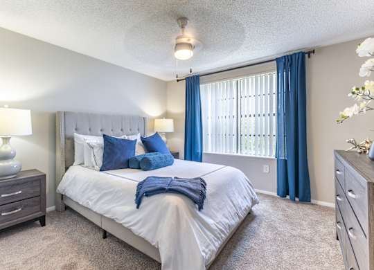 A bedroom with a large bed, a nightstand, and a window with blue curtains.