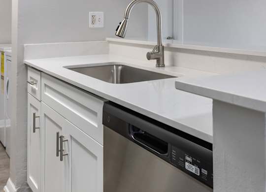 A modern kitchen with a stainless steel dishwasher and white countertops.