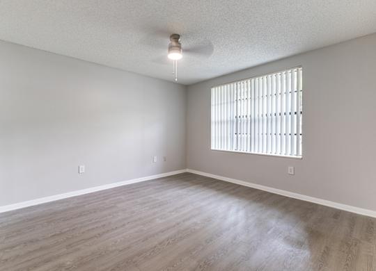 A room with a window covered by blinds and wooden flooring.