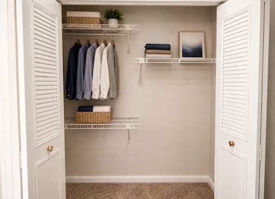 A white closet with clothes hanging and shelves with towels and a plant.