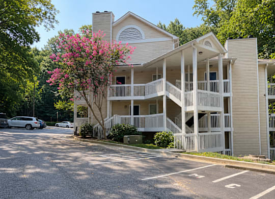 A two-story building with a balcony and a tree with pink flowers in front.