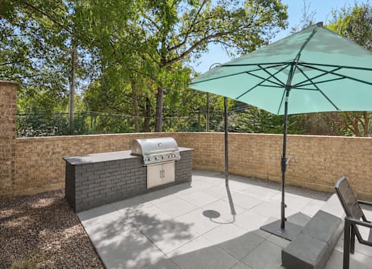 A patio with a green umbrella and a brick wall.