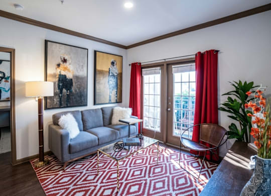 A living room with a grey couch, a red rug, and a painting on the wall.