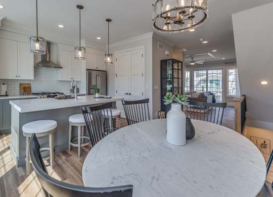 A modern dining room with round marble table and chairs with a  modern builder grade kitchen in the background,