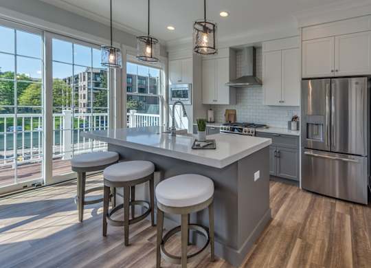 A  modern builder grade kitchen with an island with farmhouse sink and eating with with sliding glass doors in the background leading to an outdoor balcony.
