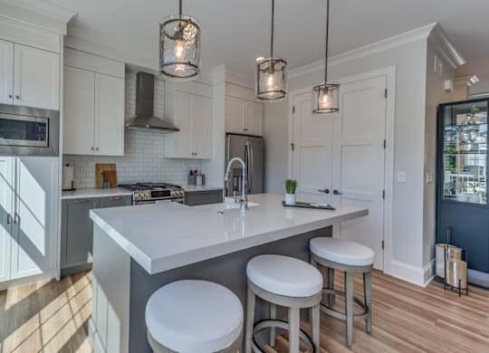 A  modern builder grade kitchen with dual tone cabinets and a large island with farmhouse sink and eating bar.