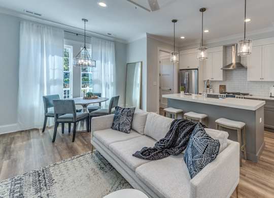 A modern builder grade living room with grey couch and dining room and kitchen in the background.