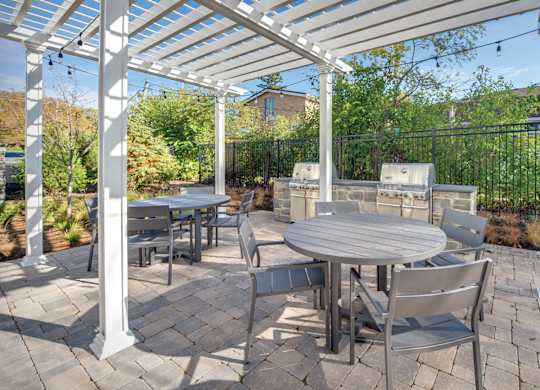 A townhome complex patio with grills, tables and chairs on a brick walkway underneath cafe lights.