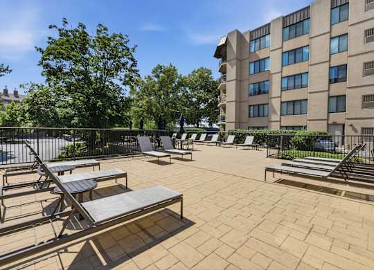 A sunny day at the outdoor seating area of a building with multiple lounge chairs and tables.