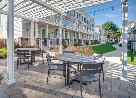 A townhome complex patio with grills, tables and chairs on a brick walkway underneath cafe lights.