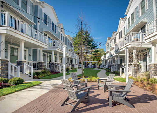 A sunny day at a townhome complex with Adirondack chairs, cafe lights, and brick walkway.
