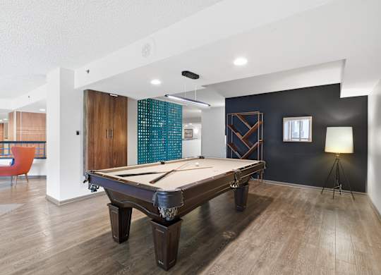 A pool table is in the middle of a room with a chair and a lamp.