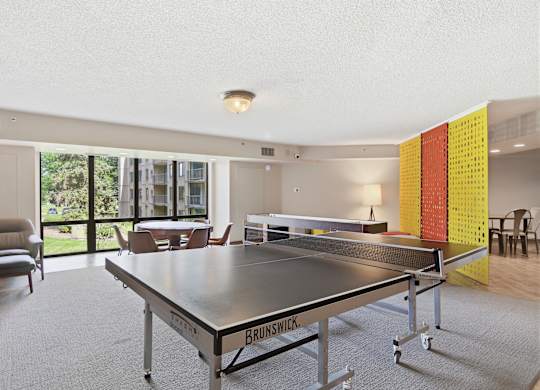 A ping pong table is in the middle of a room with a chair and a window.