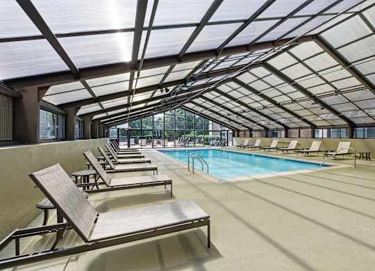 A sunroom with a pool and lounge chairs.