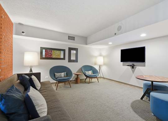 A living room with a grey couch, blue chairs, and a flat screen TV.