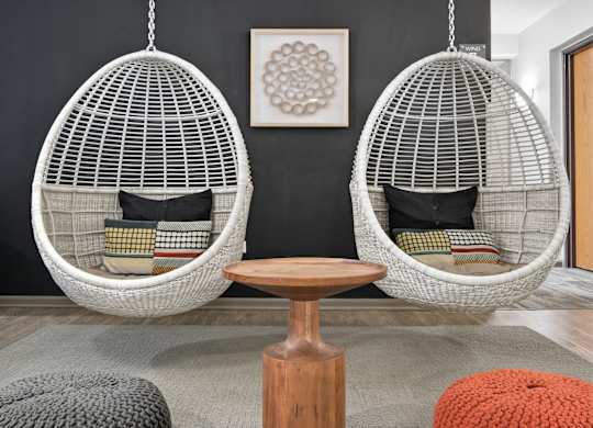 Two white hanging egg chairs with cushions and a wooden table in the middle of a room.