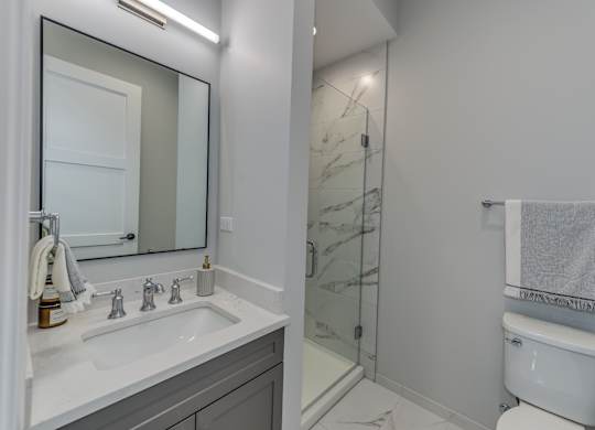 A modern builder grade bathroom with a white toilet, marble counter top vanity, and glass tiled shower.