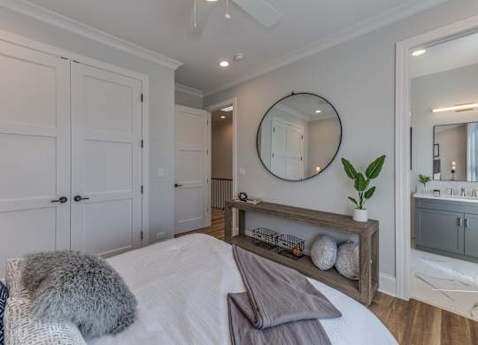 A modern builder grade bedroom with a bed, ceiling fan, and doorway into the en suite bathroom.