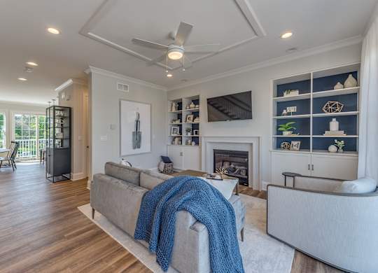 A modern builder grade living room with a fireplace with custom built ins and ceiling fan.
