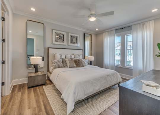 A modern builder grade bedroom with a large bed, windows, a ceiling fan, and dual side tables with lamps.