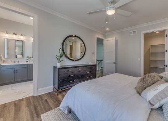 A modern builder grade bedroom with a large bed and a mirror on the wall with a doorway into the en suite bathroom and doorway with the walk in closet.