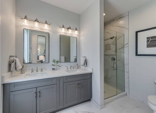 A modern builder grade bathroom with a dual vanity and a glass shower.