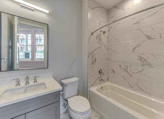 A modern builder grade bathroom with a marble tile shower and soaking tub with vanity and mirror.
