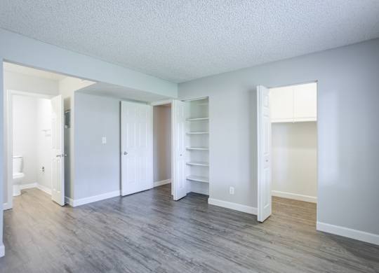 A room with white walls and wood flooring with a doorway leading to another room.