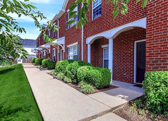 A row of red brick houses with green bushes in front.