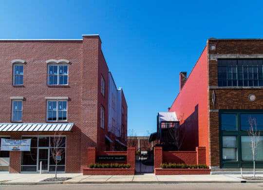 a pair of red brick apartment buildings on a street with a blue sky in the background